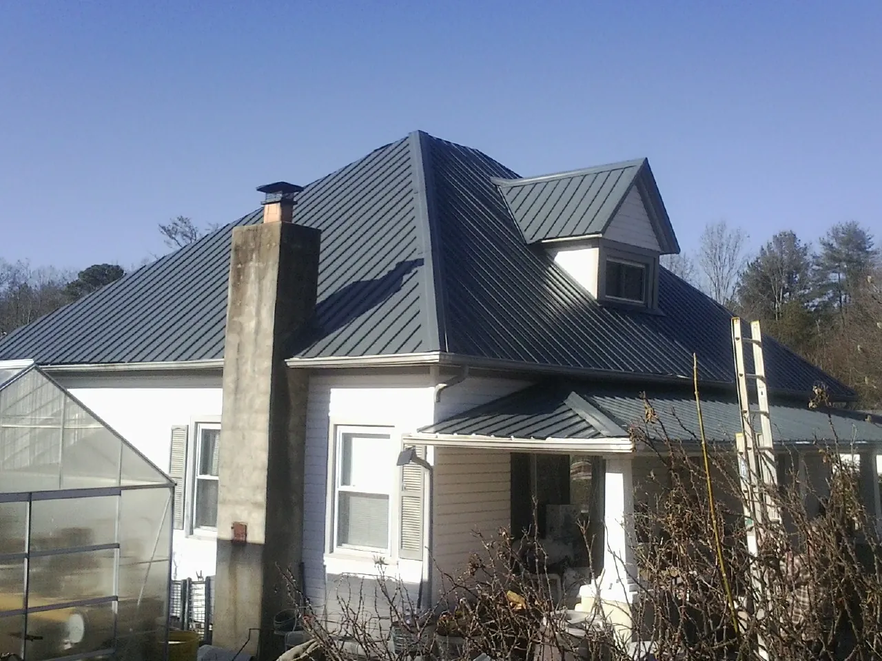 Dark blue standing seam metal roof on a white farmhouse with dormer — Slate & Tile Roof Repair by Roofing Brothers in Kellogg