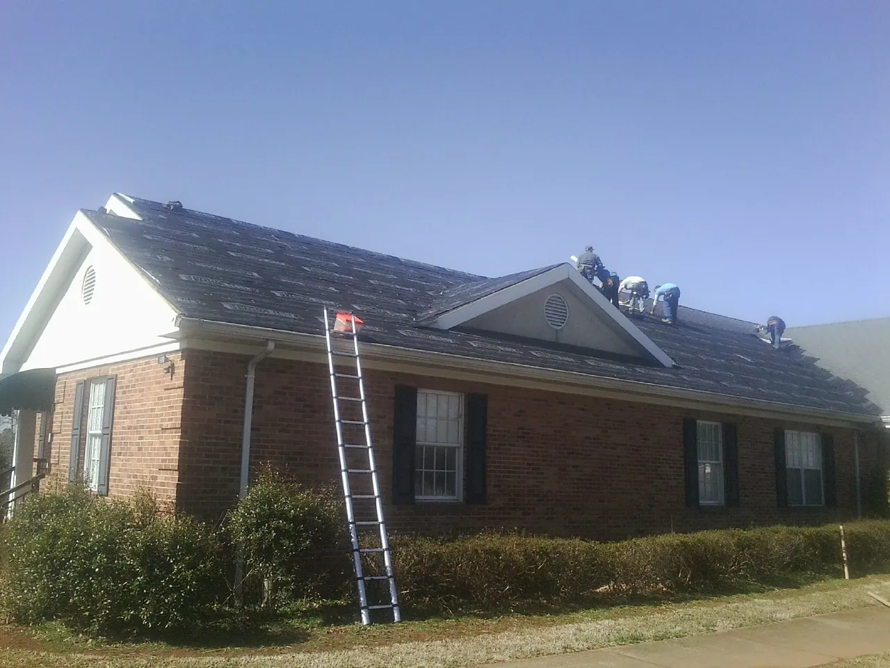 Crew tearing shingles off a brick ranch roof with a ladder set — Metal Roof Repair work by our crew in Kellogg