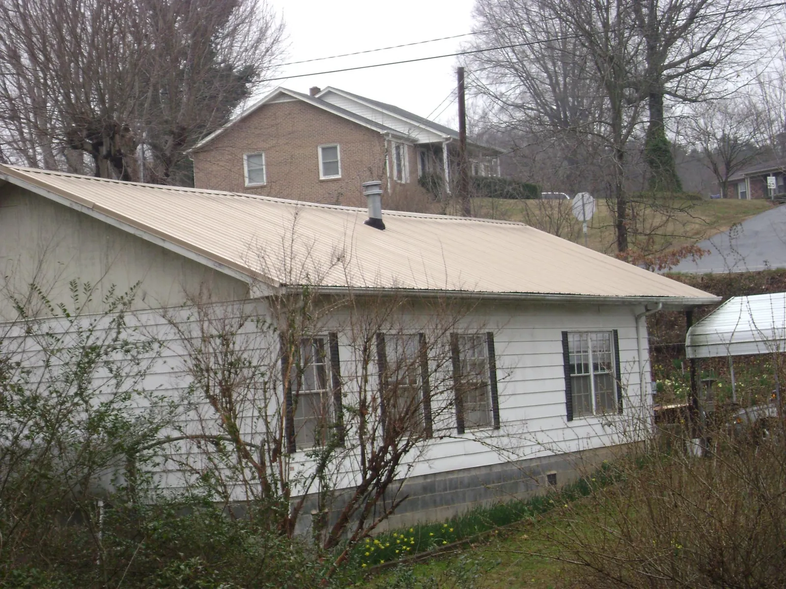 Tan metal roof on a white sided house set into a hillside — Commercial Roofing by Roofing Brothers in Kellogg